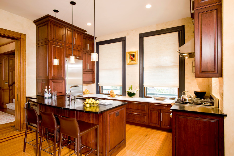 Exempel på ett mellanstort klassiskt kök, med en undermonterad diskho, luckor med upphöjd panel, bänkskiva i täljsten, vitt stänkskydd, stänkskydd i mosaik, rostfria vitvaror, mellanmörkt trägolv, en halv köksö och skåp i mörkt trä