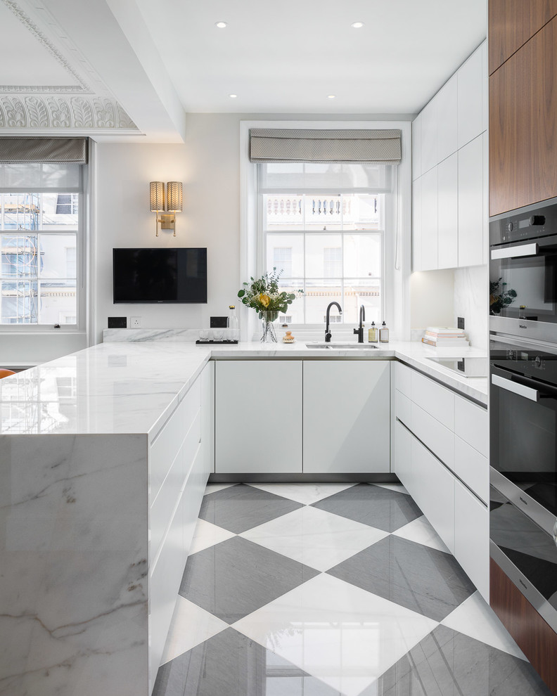 This is an example of a medium sized contemporary u-shaped open plan kitchen in Surrey with a double-bowl sink, flat-panel cabinets, white cabinets, marble worktops, white splashback, marble splashback, black appliances, marble flooring, a breakfast bar, multi-coloured floors and white worktops.