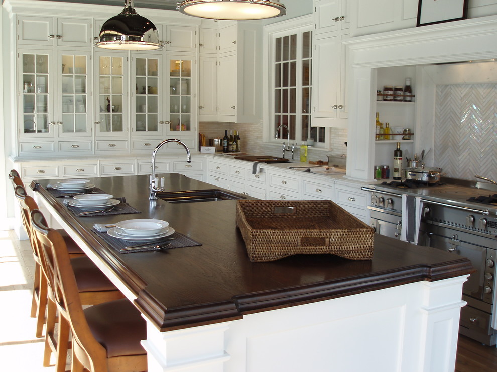 Elegant l-shaped eat-in kitchen photo in New York with glass-front cabinets, wood countertops and an undermount sink