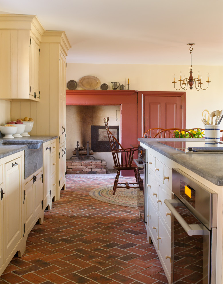 Idéer för att renovera ett mellanstort lantligt grå linjärt grått kök och matrum, med en rustik diskho, luckor med upphöjd panel, tegelgolv, en köksö, beige skåp, bänkskiva i betong, integrerade vitvaror och rött golv