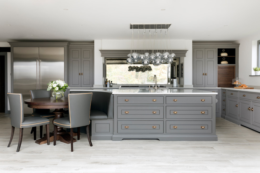Klassisk inredning av ett mellanstort l-kök, med grå skåp, rostfria vitvaror, en köksö, beiget golv och fönster som stänkskydd