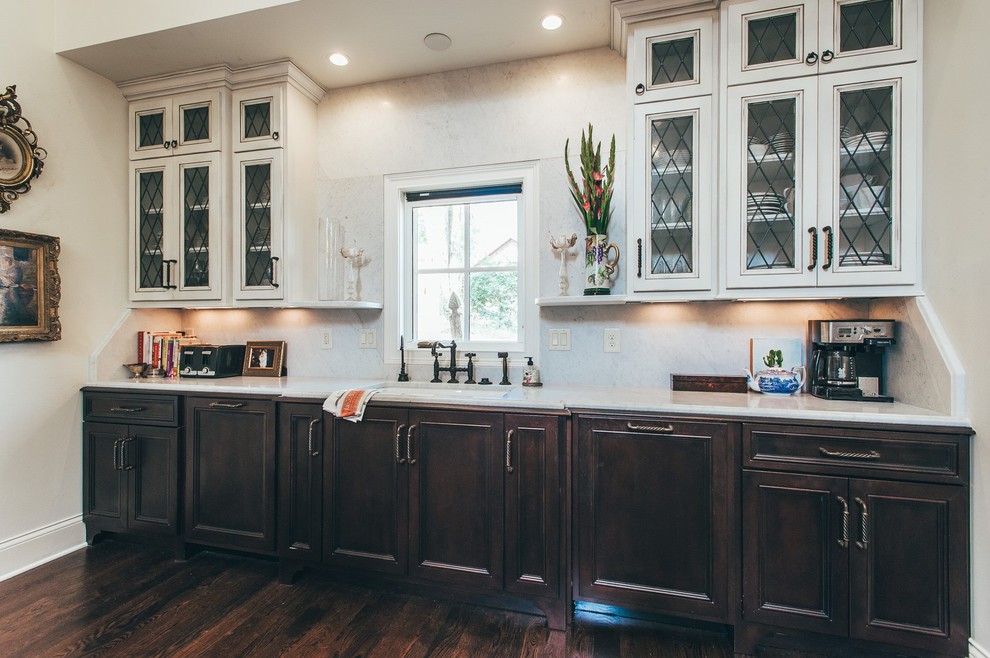 This is an example of a large traditional u-shaped kitchen/diner in Nashville with a submerged sink, glass-front cabinets, white cabinets, marble worktops, white splashback, stone slab splashback, stainless steel appliances, dark hardwood flooring and an island.