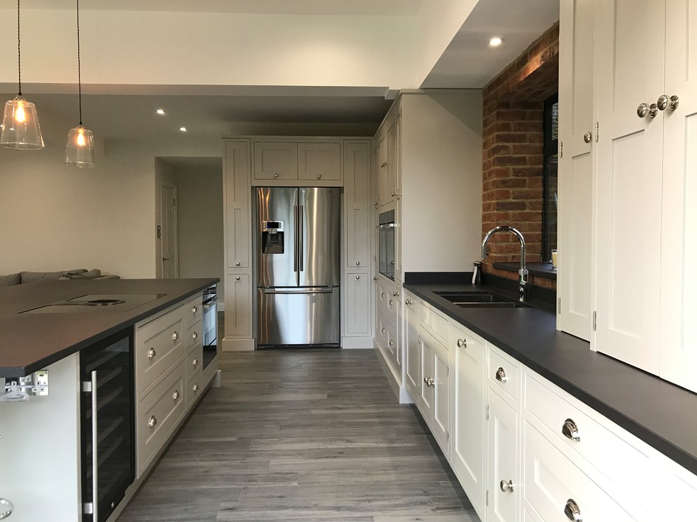 This is an example of a large classic l-shaped open plan kitchen in Surrey with an integrated sink, shaker cabinets, white cabinets, quartz worktops, stainless steel appliances, porcelain flooring, an island and grey floors.