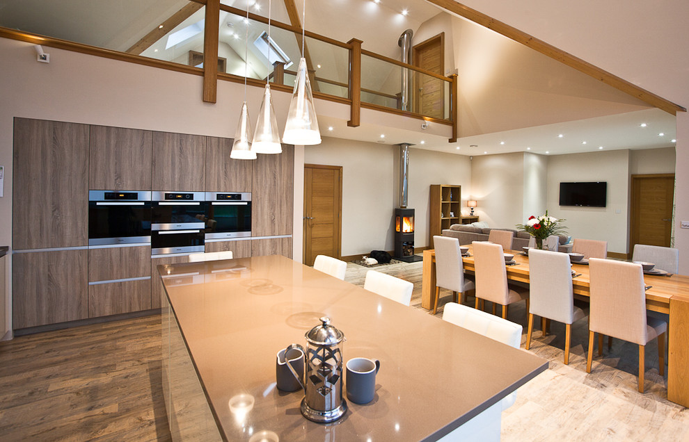 Moderne Wohnküche mit flächenbündigen Schrankfronten, hellbraunen Holzschränken, Elektrogeräten mit Frontblende, braunem Holzboden und Kücheninsel in Sonstige