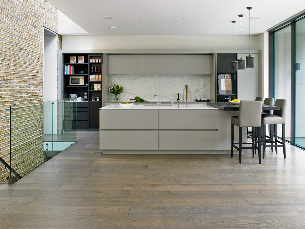 Design ideas for a contemporary kitchen in London with a submerged sink, flat-panel cabinets, grey cabinets, white splashback, black appliances, medium hardwood flooring and an island.