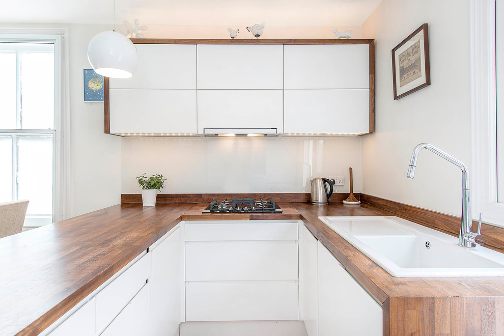 Moderne Schmale Küche in U-Form mit Einbauwaschbecken, flächenbündigen Schrankfronten, weißen Schränken, Arbeitsplatte aus Holz, Küchenrückwand in Weiß, Glasrückwand und Halbinsel in London