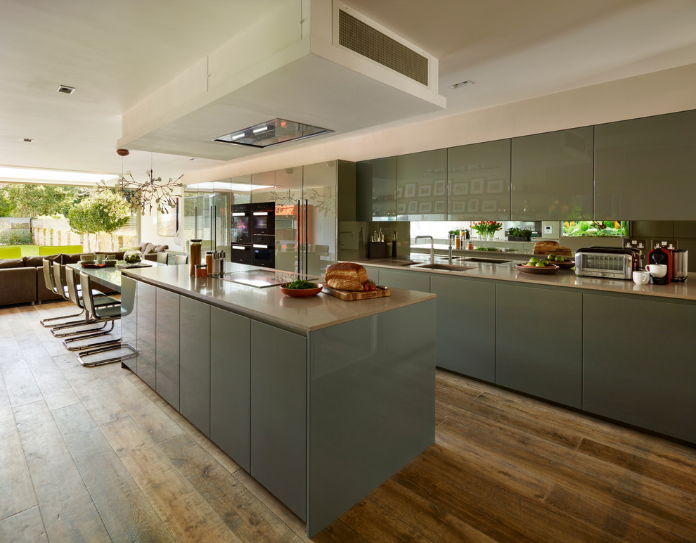 Contemporary open plan kitchen in London with flat-panel cabinets, medium hardwood flooring and an island.