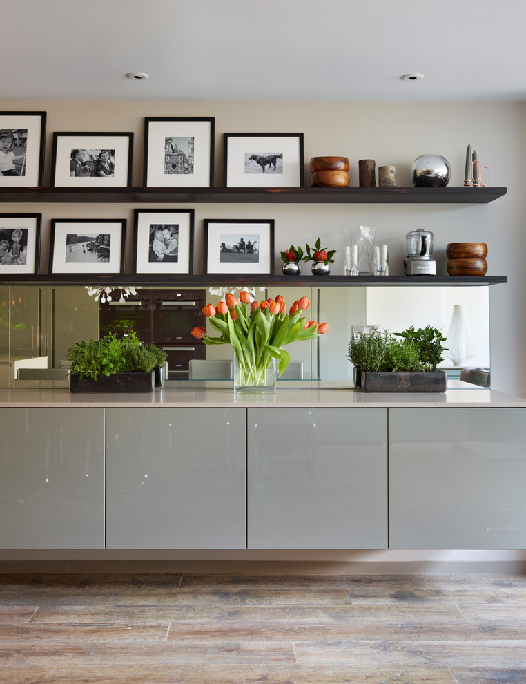 Offene Moderne Küche mit flächenbündigen Schrankfronten, Mineralwerkstoff-Arbeitsplatte, Rückwand aus Spiegelfliesen, braunem Holzboden und Kücheninsel in London
