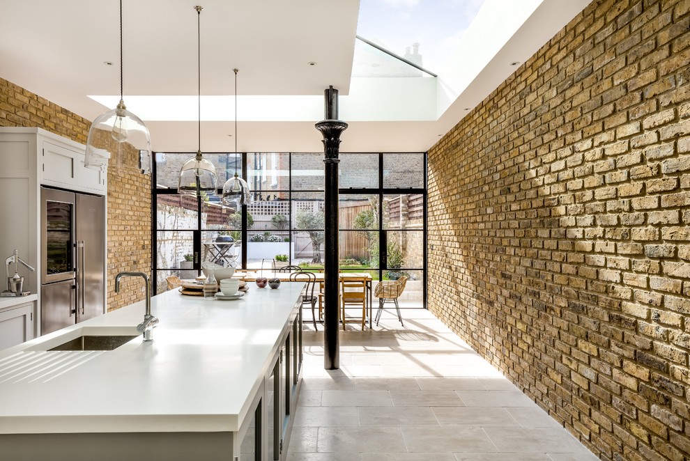 Inspiration for a mid-sized contemporary single-wall limestone floor eat-in kitchen remodel in London with an integrated sink, shaker cabinets, gray cabinets, solid surface countertops, glass sheet backsplash, stainless steel appliances and an island