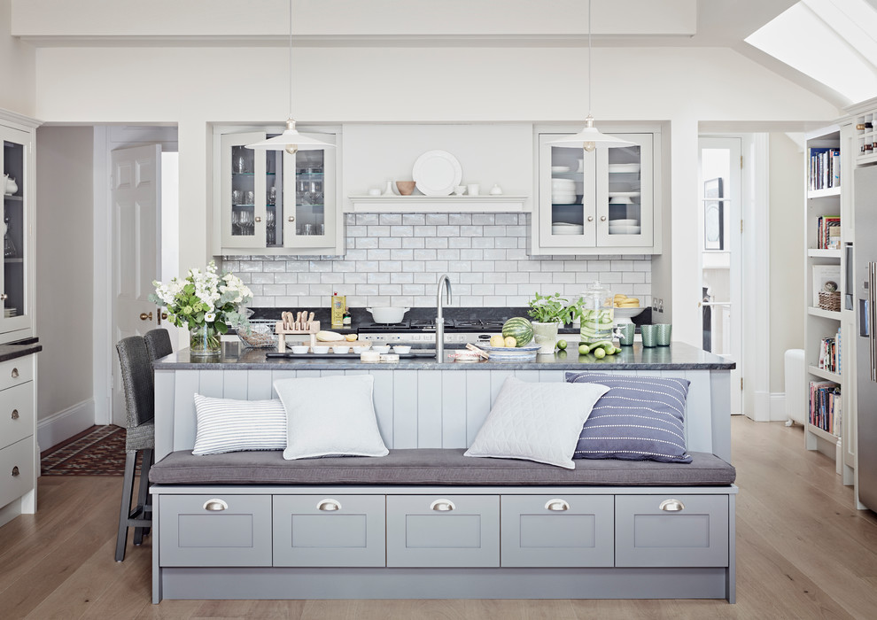 Modern inredning av ett kök, med en undermonterad diskho, vita skåp, vitt stänkskydd, stänkskydd i tunnelbanekakel, ljust trägolv, en köksö, beiget golv, granitbänkskiva och skåp i shakerstil