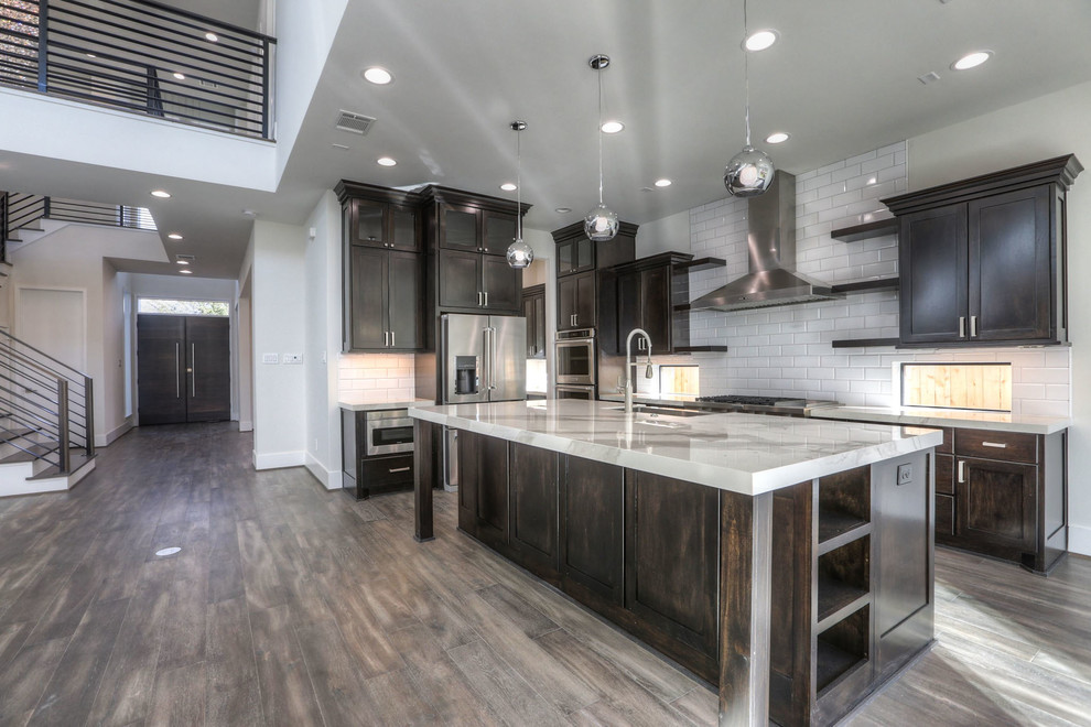 Photo of a large traditional l-shaped open plan kitchen in Houston with a belfast sink, shaker cabinets, dark wood cabinets, marble worktops, white splashback, metro tiled splashback, stainless steel appliances, dark hardwood flooring, an island and brown floors.