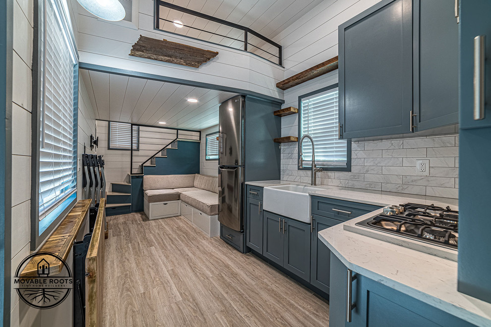 Example of a small minimalist l-shaped vinyl floor and beige floor open concept kitchen design in Dallas with a farmhouse sink, shaker cabinets, blue cabinets, quartz countertops, gray backsplash, porcelain backsplash, stainless steel appliances, no island and white countertops