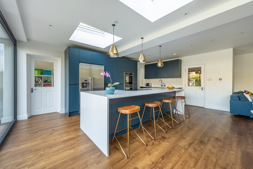 Example of a large minimalist vinyl floor open concept kitchen design in London with a drop-in sink, flat-panel cabinets, blue cabinets, quartzite countertops, white backsplash, subway tile backsplash, stainless steel appliances, an island and white countertops