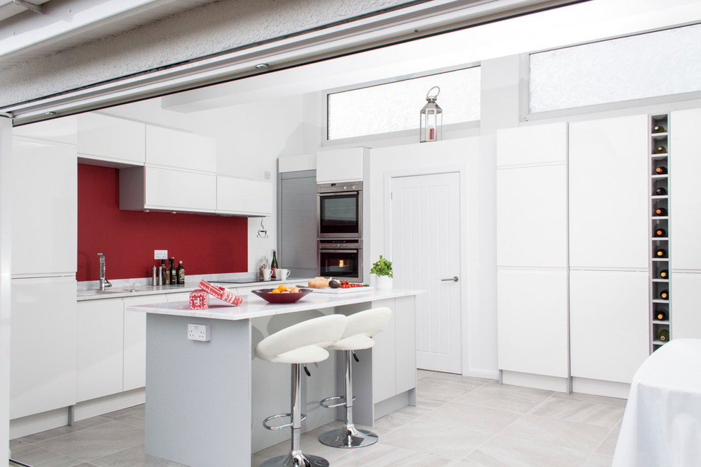 Bild på ett litet industriellt kök, med släta luckor, vita skåp, en köksö, en nedsänkt diskho, bänkskiva i koppar, rött stänkskydd, rostfria vitvaror och klinkergolv i keramik