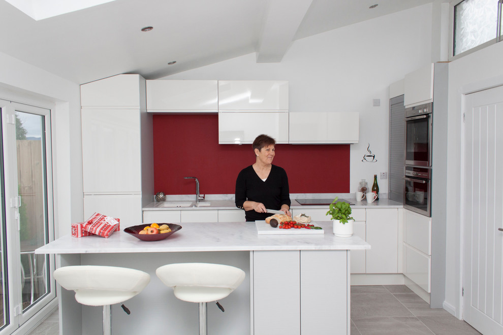 Inredning av ett modernt litet kök, med en nedsänkt diskho, släta luckor, vita skåp, bänkskiva i koppar, rött stänkskydd, rostfria vitvaror, klinkergolv i keramik och en köksö