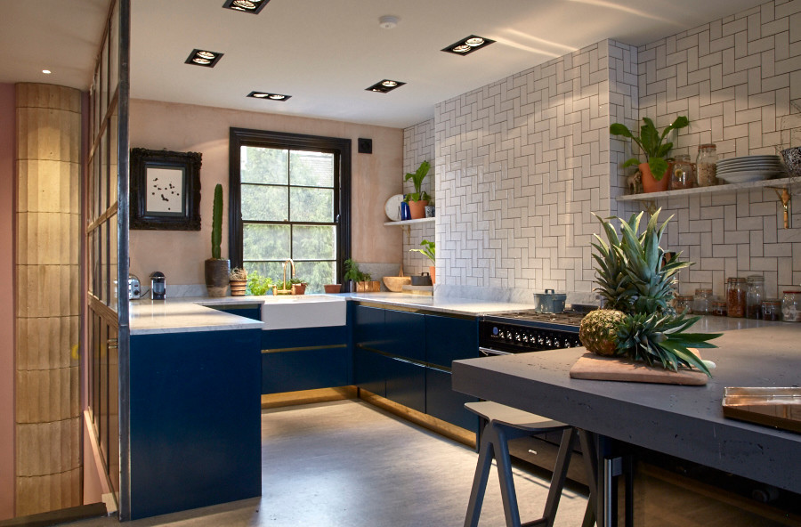 Inspiration for a medium sized bohemian u-shaped kitchen in London with a belfast sink, flat-panel cabinets, blue cabinets, marble worktops, white splashback, ceramic splashback, black appliances and concrete flooring.
