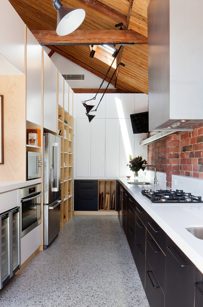 Ejemplo de cocina lineal industrial sin isla con armarios con paneles lisos, puertas de armario negras y electrodomésticos de acero inoxidable