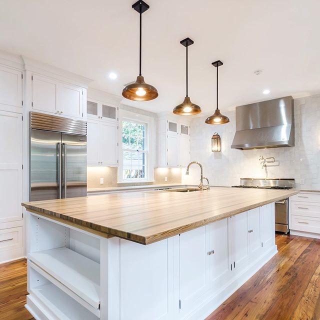 Example of a large country l-shaped medium tone wood floor and brown floor kitchen design in New Orleans with an island, white cabinets, wood countertops, white backsplash, stainless steel appliances and brown countertops