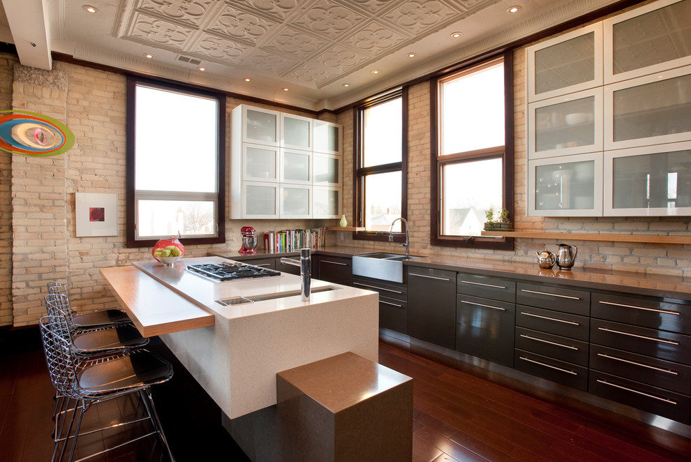 Geräumige Moderne Wohnküche in U-Form mit Küchengeräten aus Edelstahl, Glasfronten, grauen Schränken, Quarzit-Arbeitsplatte, Kücheninsel, Landhausspüle und braunem Holzboden in Sonstige