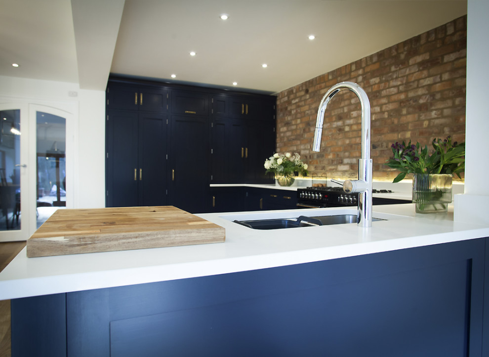 Design ideas for a medium sized industrial l-shaped open plan kitchen in Other with a submerged sink, shaker cabinets, black cabinets, composite countertops, brick splashback, black appliances, light hardwood flooring, no island, beige floors and white worktops.