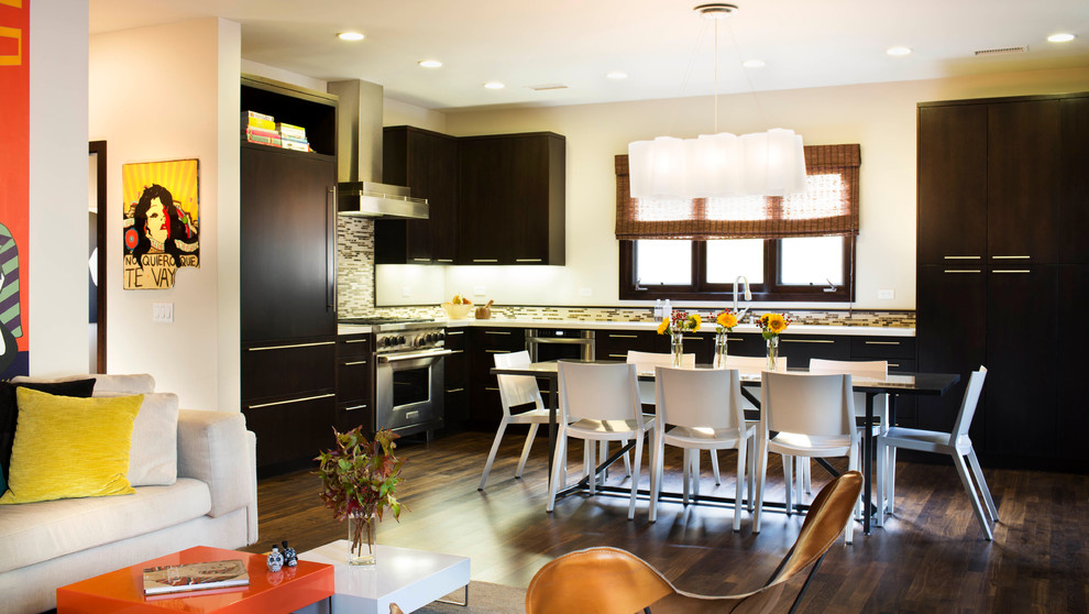 На фото: угловая кухня-гостиная в современном стиле с плоскими фасадами, темными деревянными фасадами, разноцветным фартуком и техникой под мебельный фасад с