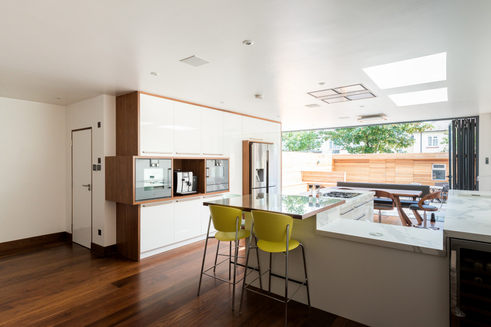 Immagine di una cucina design con ante lisce, ante bianche, elettrodomestici in acciaio inossidabile, parquet scuro, pavimento marrone e top bianco