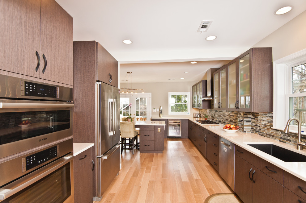 This is an example of a large contemporary kitchen/diner in DC Metro with a single-bowl sink, flat-panel cabinets, grey cabinets, engineered stone countertops, green splashback, mosaic tiled splashback, stainless steel appliances, light hardwood flooring, an island, brown floors and beige worktops.