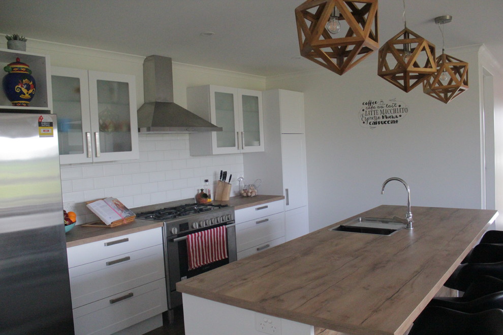 Medium sized traditional galley kitchen pantry in Christchurch with a built-in sink, recessed-panel cabinets, white cabinets, laminate countertops, white splashback, metro tiled splashback, stainless steel appliances, laminate floors and brown floors.