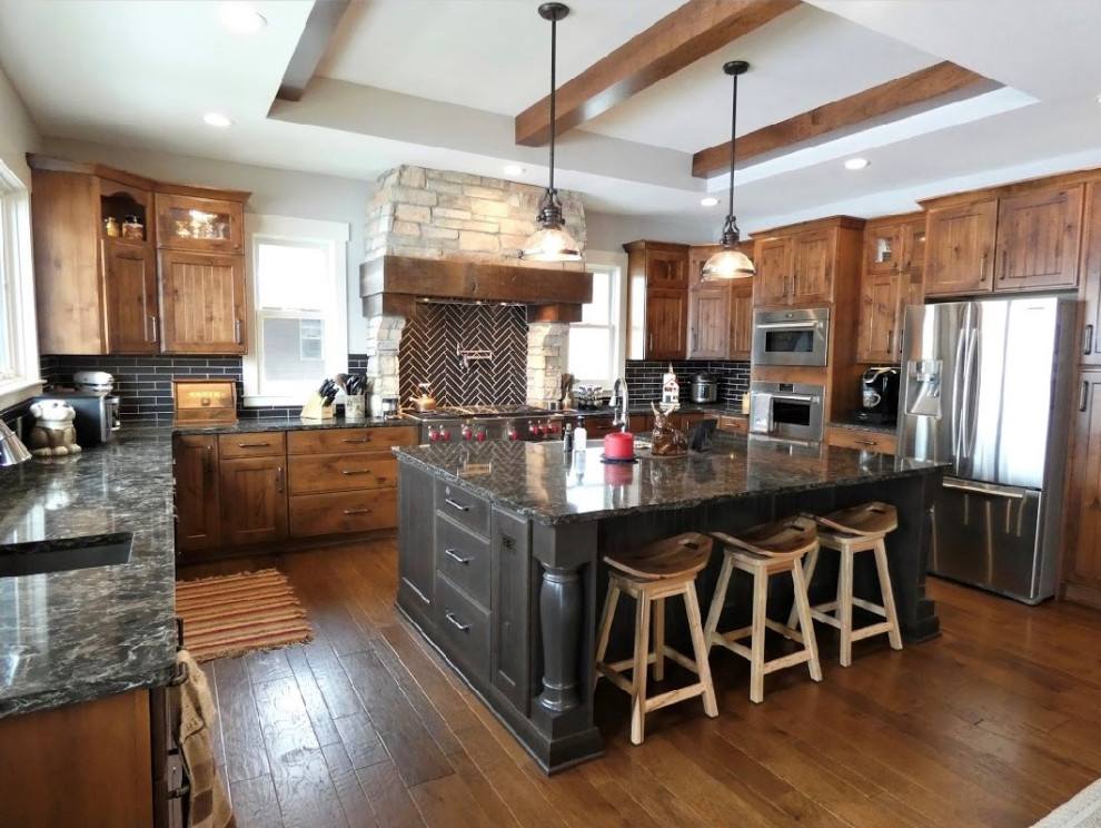 Bild på ett rustikt brun brunt kök, med en rustik diskho, luckor med infälld panel, skåp i mörkt trä, bänkskiva i kvarts, svart stänkskydd, stänkskydd i travertin, rostfria vitvaror och en köksö