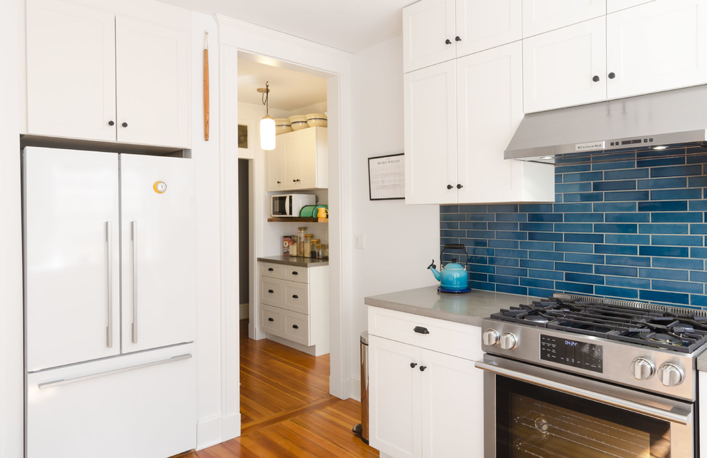 ボストンにある高級な中くらいなエクレクティックスタイルのおしゃれなキッチン (アンダーカウンターシンク、落し込みパネル扉のキャビネット、白いキャビネット、コンクリートカウンター、青いキッチンパネル、サブウェイタイルのキッチンパネル、白い調理設備、淡色無垢フローリング、アイランドなし、茶色い床) の写真