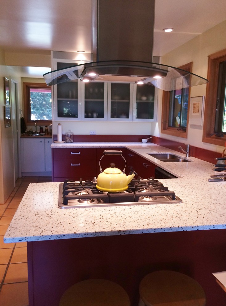 Large contemporary u-shaped kitchen in Vancouver with a submerged sink, flat-panel cabinets, red cabinets, recycled glass countertops, red splashback and terracotta flooring.