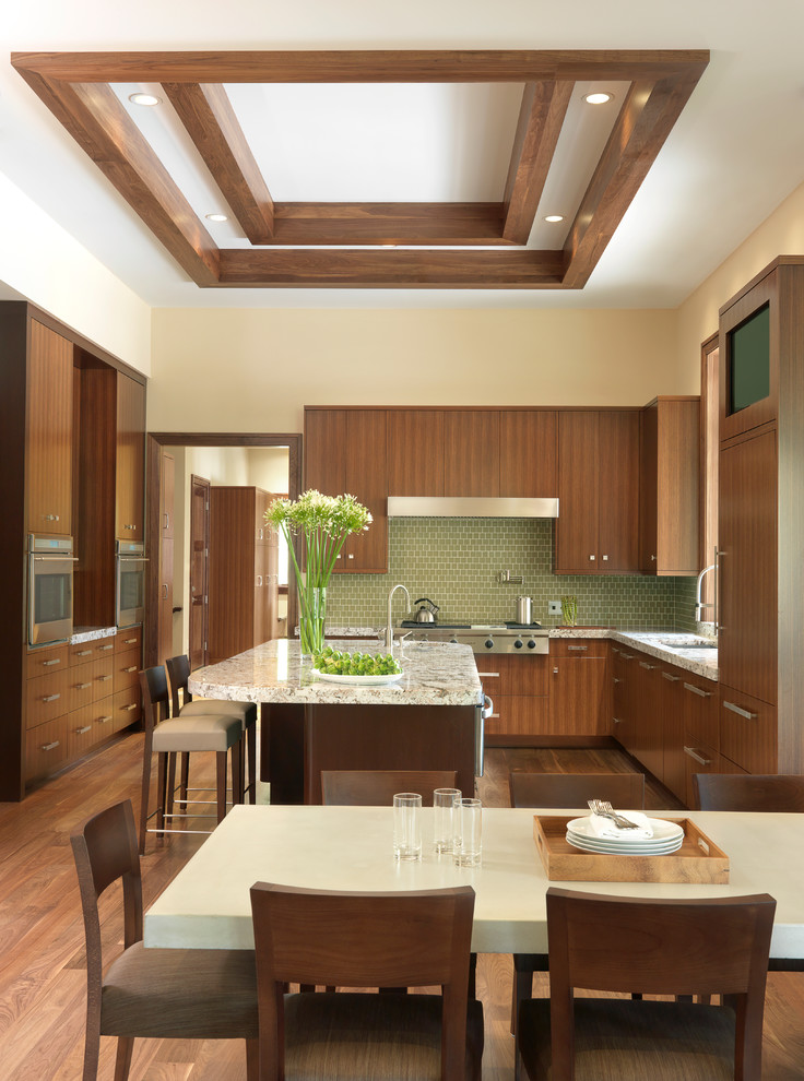 Exemple d'une cuisine américaine tendance en U et bois brun avec îlot, un placard à porte plane, une crédence en céramique, un électroménager en acier inoxydable, un évier encastré, un sol en bois brun et une crédence verte.