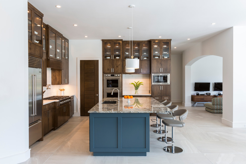 Inspiration for a transitional l-shaped porcelain tile enclosed kitchen remodel in Houston with an undermount sink, flat-panel cabinets, medium tone wood cabinets, granite countertops, white backsplash, ceramic backsplash, stainless steel appliances and an island