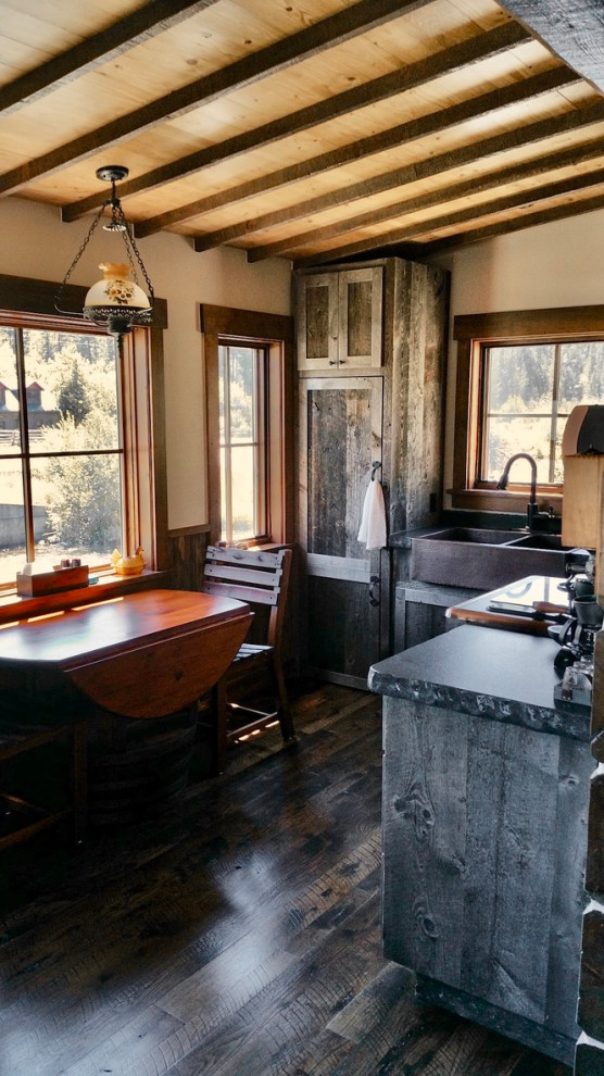 This is an example of a small rustic l-shaped kitchen/diner in Other with a belfast sink, shaker cabinets, distressed cabinets, granite worktops, black appliances, dark hardwood flooring and no island.