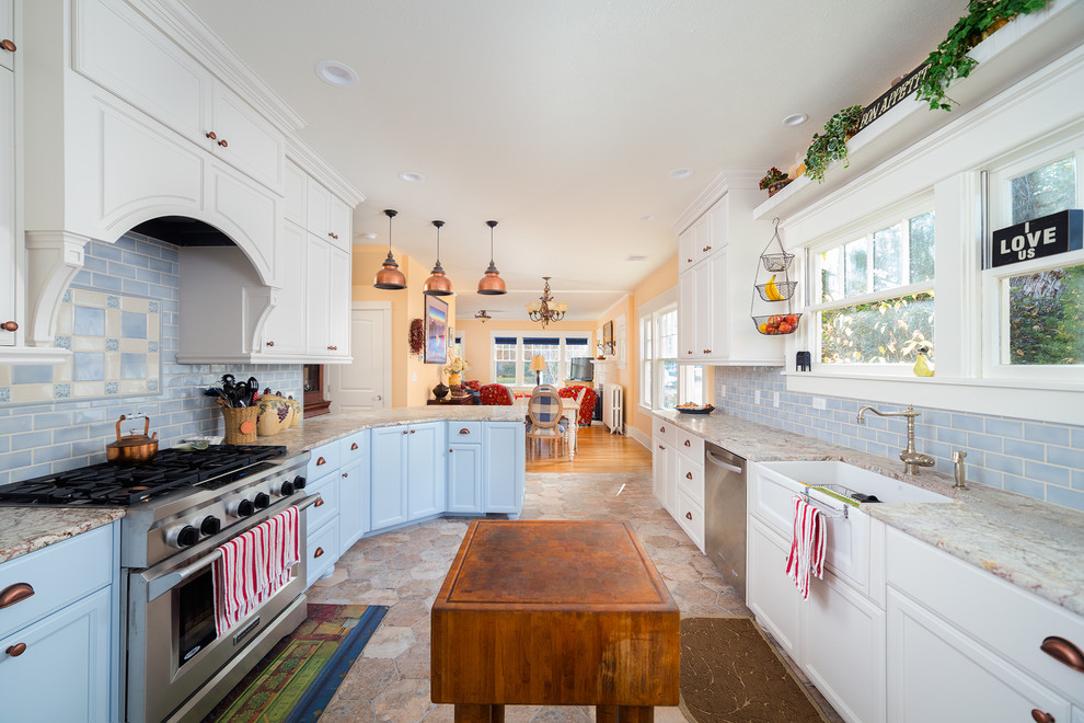 Bild på ett lantligt u-kök, med en rustik diskho, luckor med infälld panel, vita skåp, blått stänkskydd, stänkskydd i tunnelbanekakel, rostfria vitvaror, en köksö och beiget golv