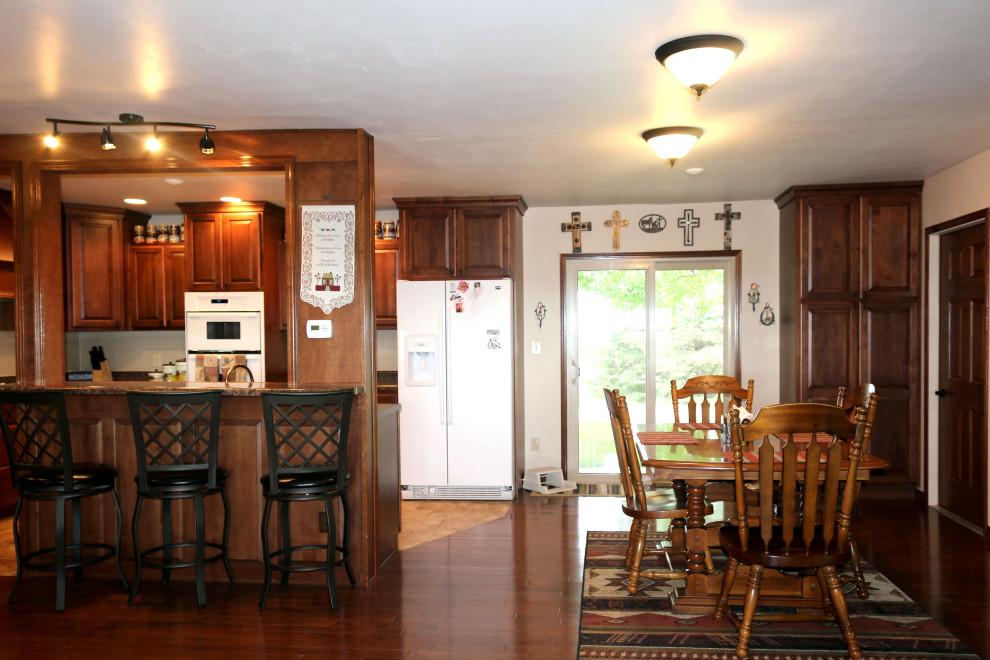 Bild på ett mellanstort vintage brun brunt kök, med en undermonterad diskho, luckor med upphöjd panel, bruna skåp, granitbänkskiva, vitt stänkskydd, stänkskydd i keramik, vita vitvaror, klinkergolv i keramik, en köksö och beiget golv