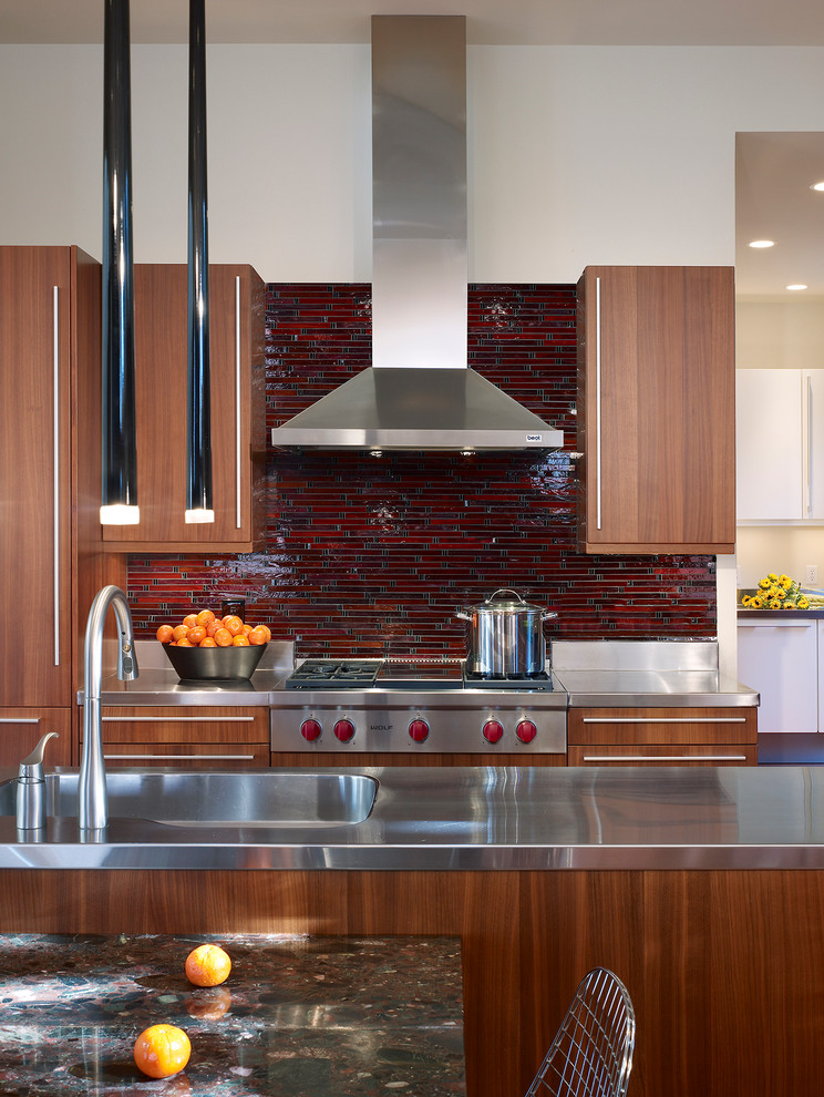 На фото: кухня в стиле модернизм с столешницей из нержавеющей стали, красным фартуком, фартуком из плитки мозаики, паркетным полом среднего тона и островом
