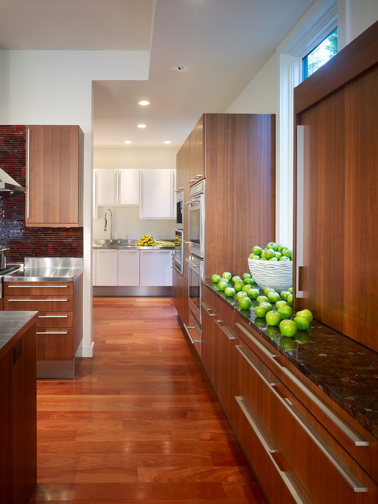Aménagement d'une cuisine moderne avec un plan de travail en inox, une crédence rouge, une crédence en mosaïque, un sol en bois brun et îlot.