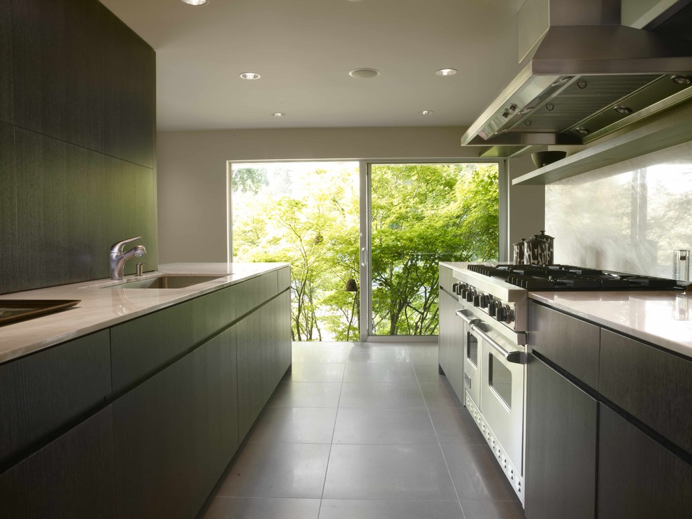 На фото: параллельная, отдельная кухня в стиле модернизм с техникой из нержавеющей стали, врезной мойкой, плоскими фасадами, черными фасадами, белым фартуком и фартуком из каменной плиты