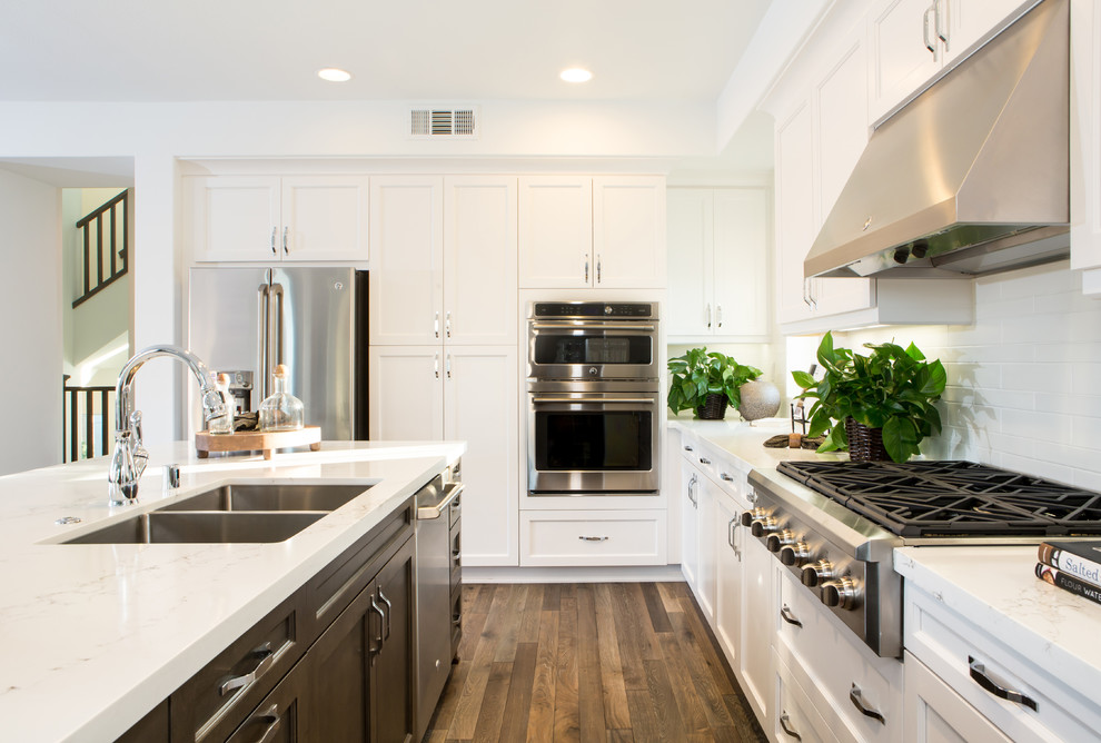 Bild på ett avskilt funkis l-kök, med en undermonterad diskho, skåp i shakerstil, vita skåp, bänkskiva i kvarts, vitt stänkskydd, rostfria vitvaror, mellanmörkt trägolv och en köksö