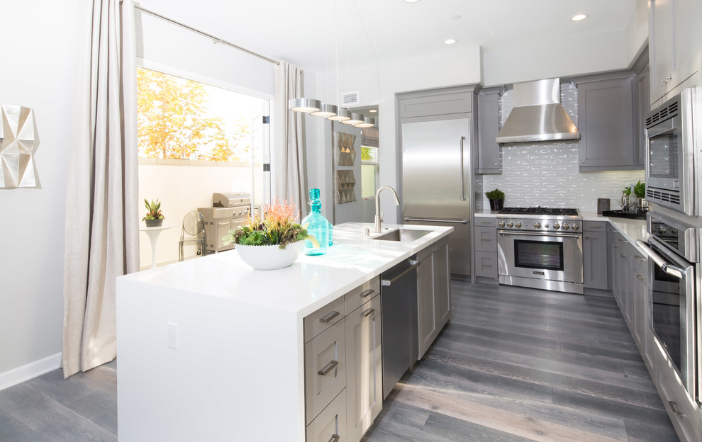 Inspiration for a contemporary l-shaped light wood floor open concept kitchen remodel in Orange County with an undermount sink, shaker cabinets, gray cabinets, quartz countertops, white backsplash, stainless steel appliances and an island