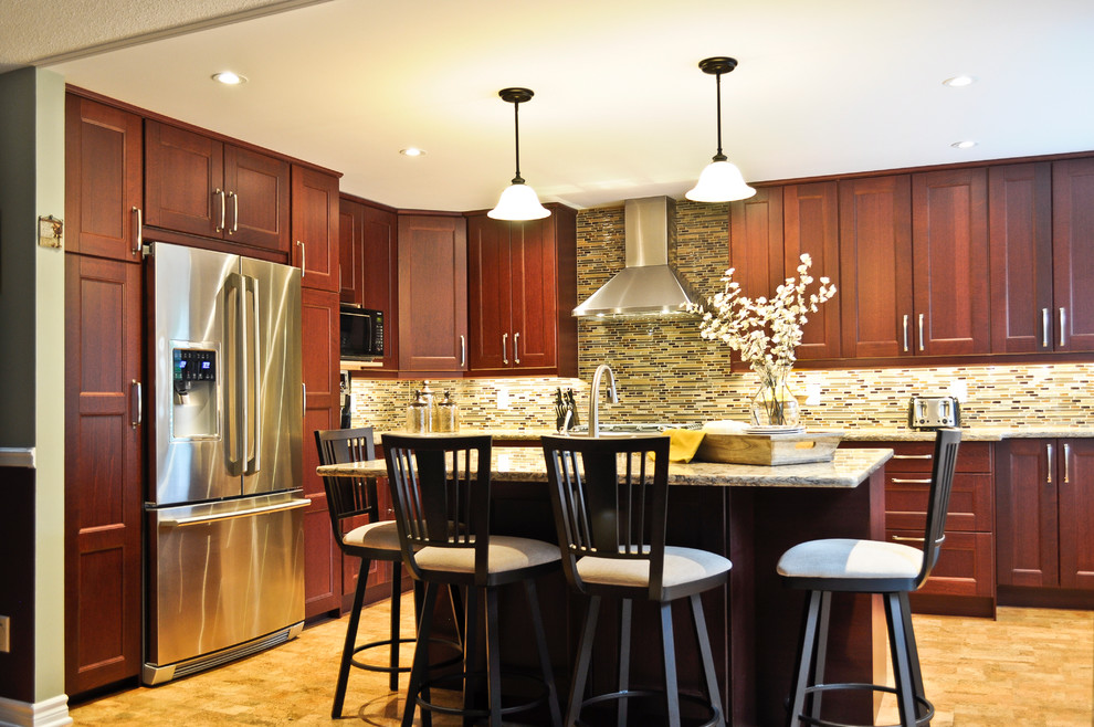 Klassisk inredning av ett kök, med luckor med infälld panel, bruna skåp, bänkskiva i kvartsit, flerfärgad stänkskydd, stänkskydd i mosaik, rostfria vitvaror, korkgolv och en köksö