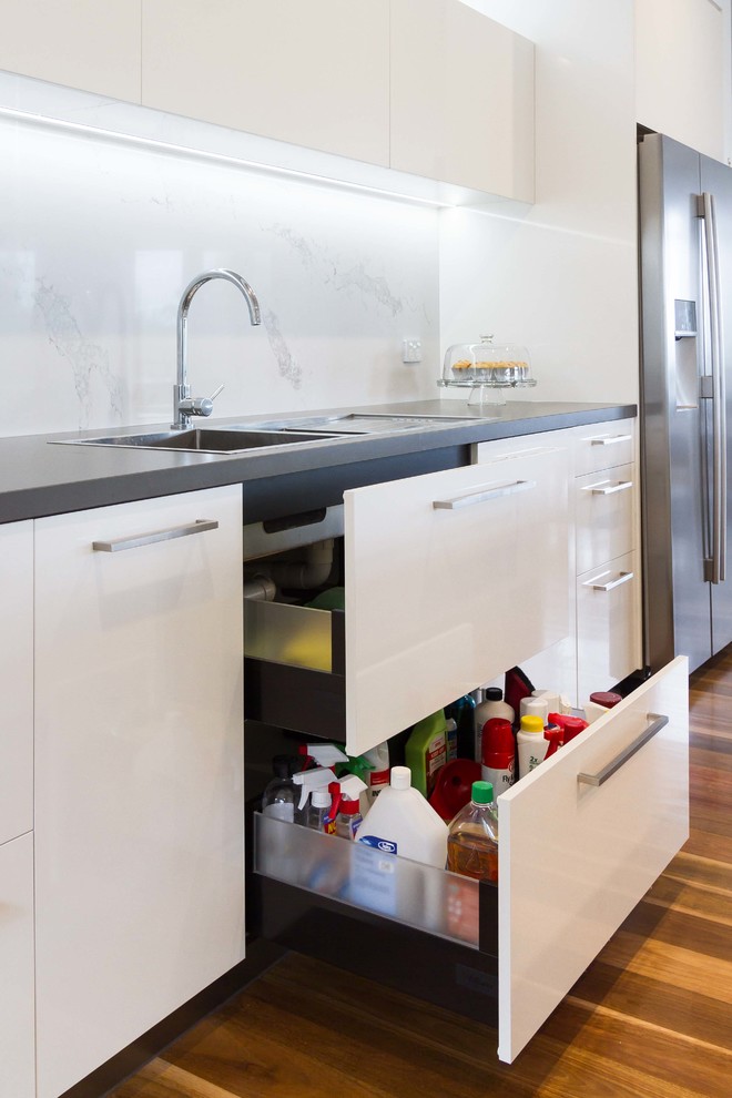 Inspiration for a large modern galley medium tone wood floor open concept kitchen remodel in Melbourne with a drop-in sink, flat-panel cabinets, white cabinets, quartz countertops, stone slab backsplash, stainless steel appliances and an island