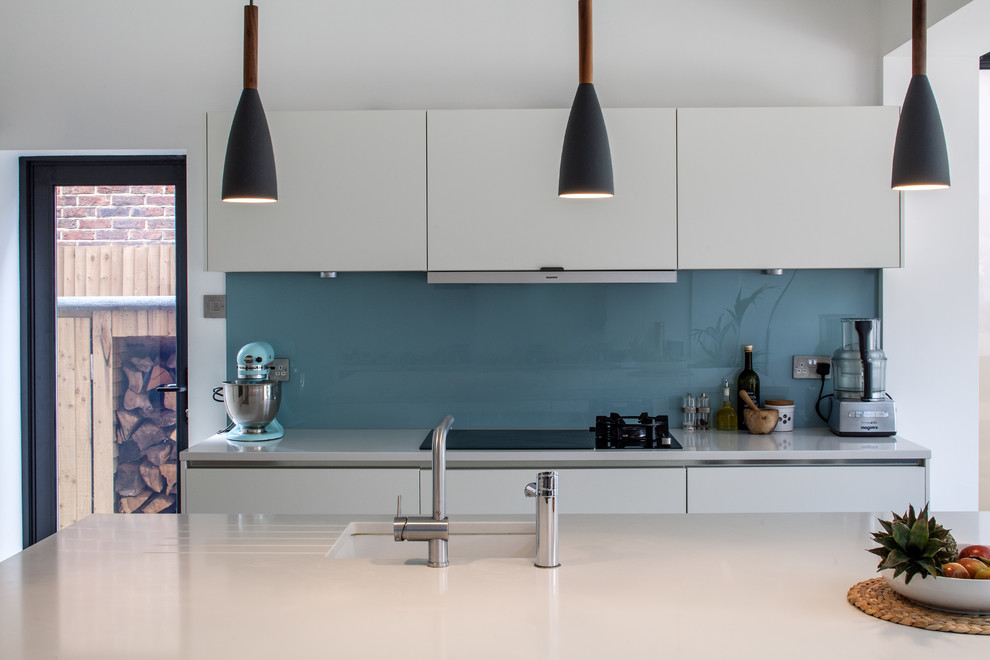 Immagine di una grande cucina minimal con ante lisce, ante bianche, top in quarzite, paraspruzzi blu, paraspruzzi con lastra di vetro, pavimento in legno massello medio e elettrodomestici in acciaio inossidabile