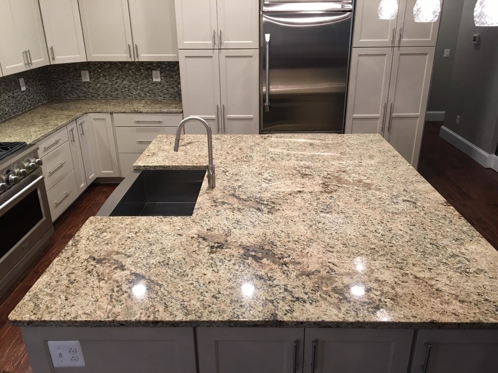 Example of a mid-sized classic u-shaped medium tone wood floor enclosed kitchen design in DC Metro with a farmhouse sink, shaker cabinets, white cabinets, granite countertops, multicolored backsplash, mosaic tile backsplash, stainless steel appliances and an island