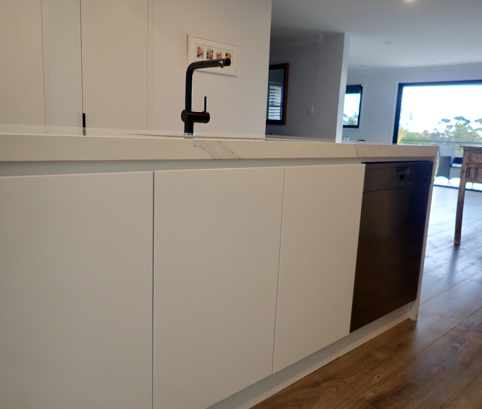 Design ideas for a large contemporary galley kitchen/diner in Sydney with a submerged sink, flat-panel cabinets, white cabinets, engineered stone countertops, white splashback, stone slab splashback, black appliances, medium hardwood flooring, an island and white worktops.