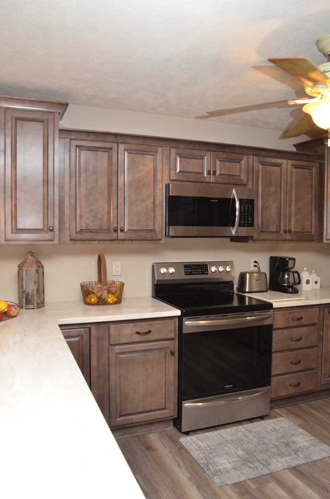 Photo of a large country u-shaped kitchen/diner in Other with a submerged sink, raised-panel cabinets, brown cabinets, composite countertops, stainless steel appliances, a breakfast bar and beige worktops.