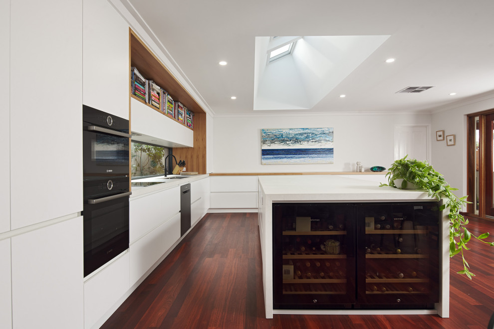 Example of a large minimalist l-shaped dark wood floor and brown floor eat-in kitchen design in Perth with an undermount sink, flat-panel cabinets, white cabinets, quartz countertops, white backsplash, window backsplash, black appliances, an island and white countertops
