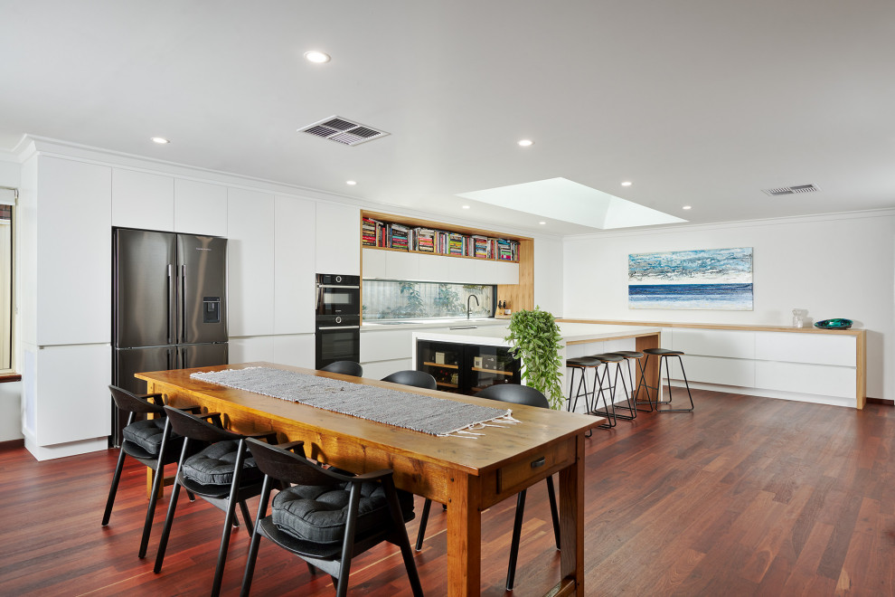 Design ideas for a large modern l-shaped kitchen/diner in Perth with a submerged sink, flat-panel cabinets, white cabinets, engineered stone countertops, white splashback, window splashback, black appliances, dark hardwood flooring, an island, brown floors and white worktops.