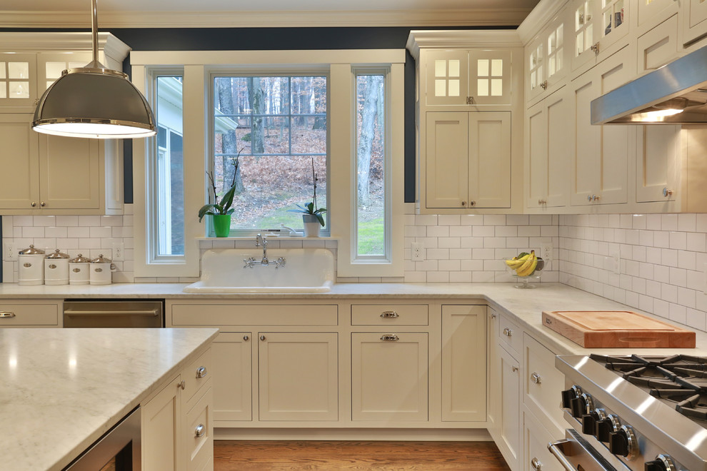 Cette image montre une cuisine traditionnelle avec un placard à porte shaker, des portes de placard blanches, une crédence blanche, une crédence en carrelage métro, un électroménager en acier inoxydable, un sol en bois brun et îlot.